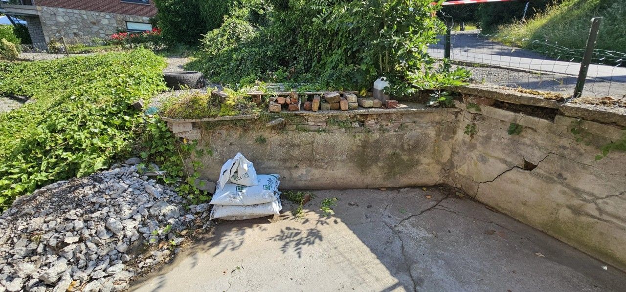 Vue d’ensemble d’un mur de soutènement existant à Housse présentant plusieurs fissures, ouvertures localisées et dégradations du parement.