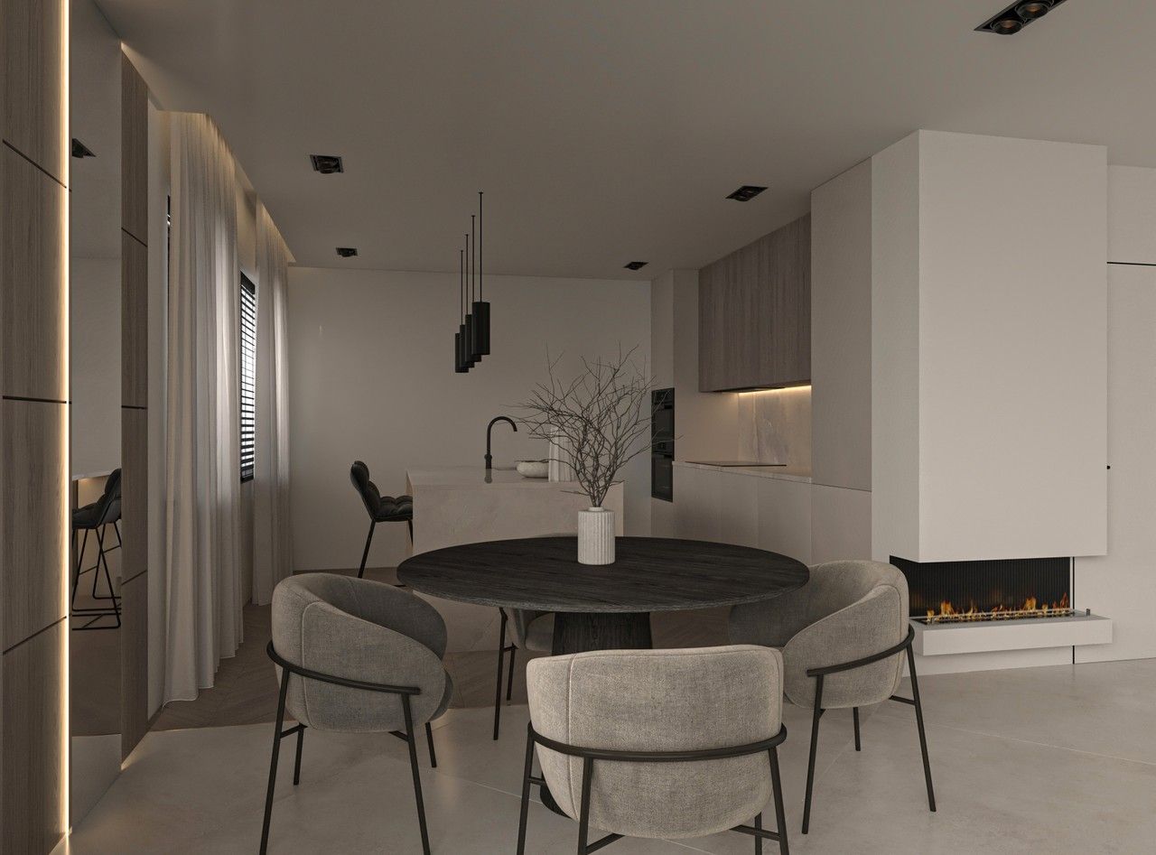 Vue de la salle à manger d’un appartement rénové à Liège, avec table ronde sombre, fauteuils rembourrés, cheminée contemporaine et cuisine ouverte en arrière-plan.
