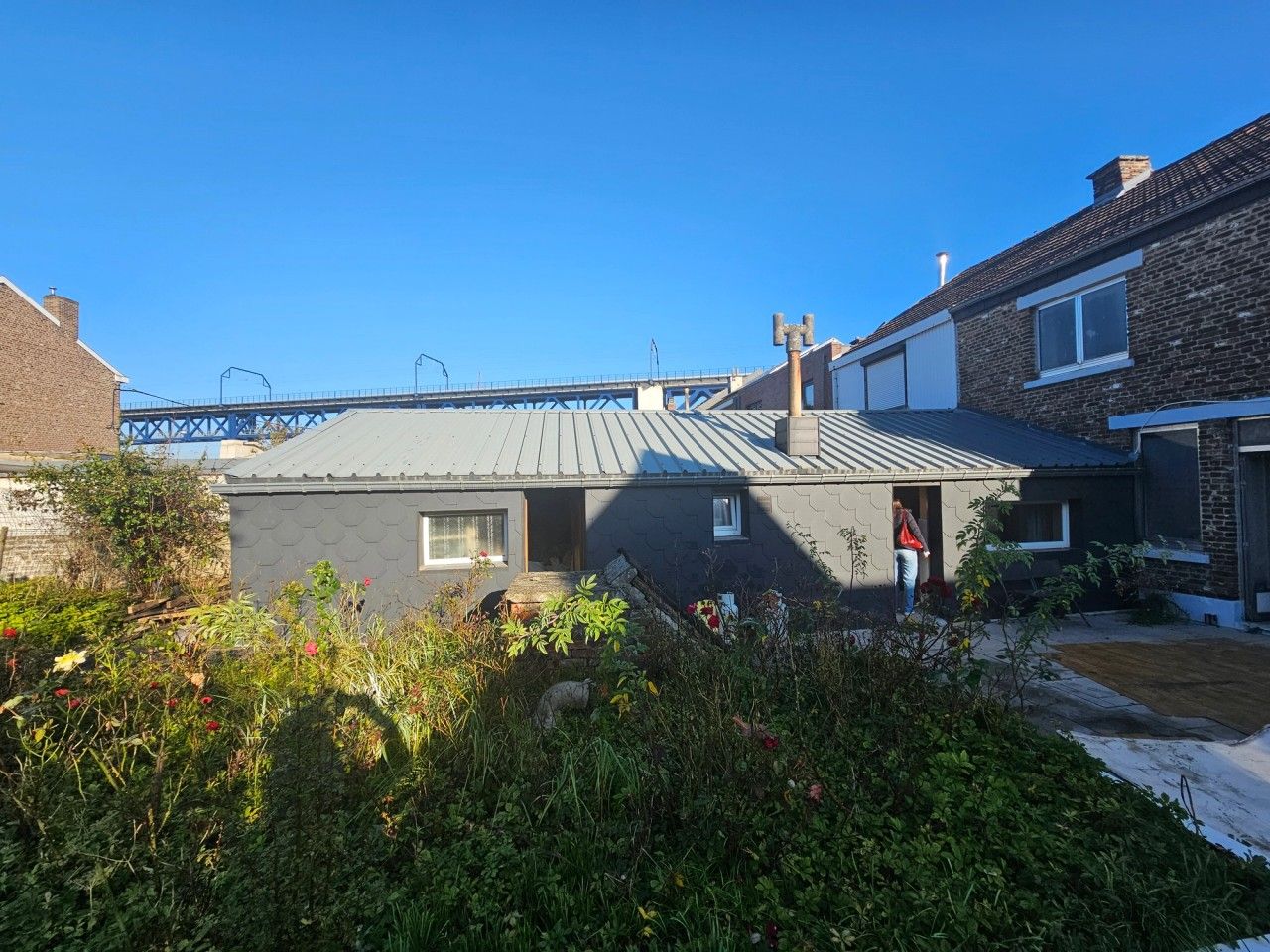 Vue de l’annexe arrière existante d’une maison à Visé, avec toiture métallique inclinée et jardin avant transformation.