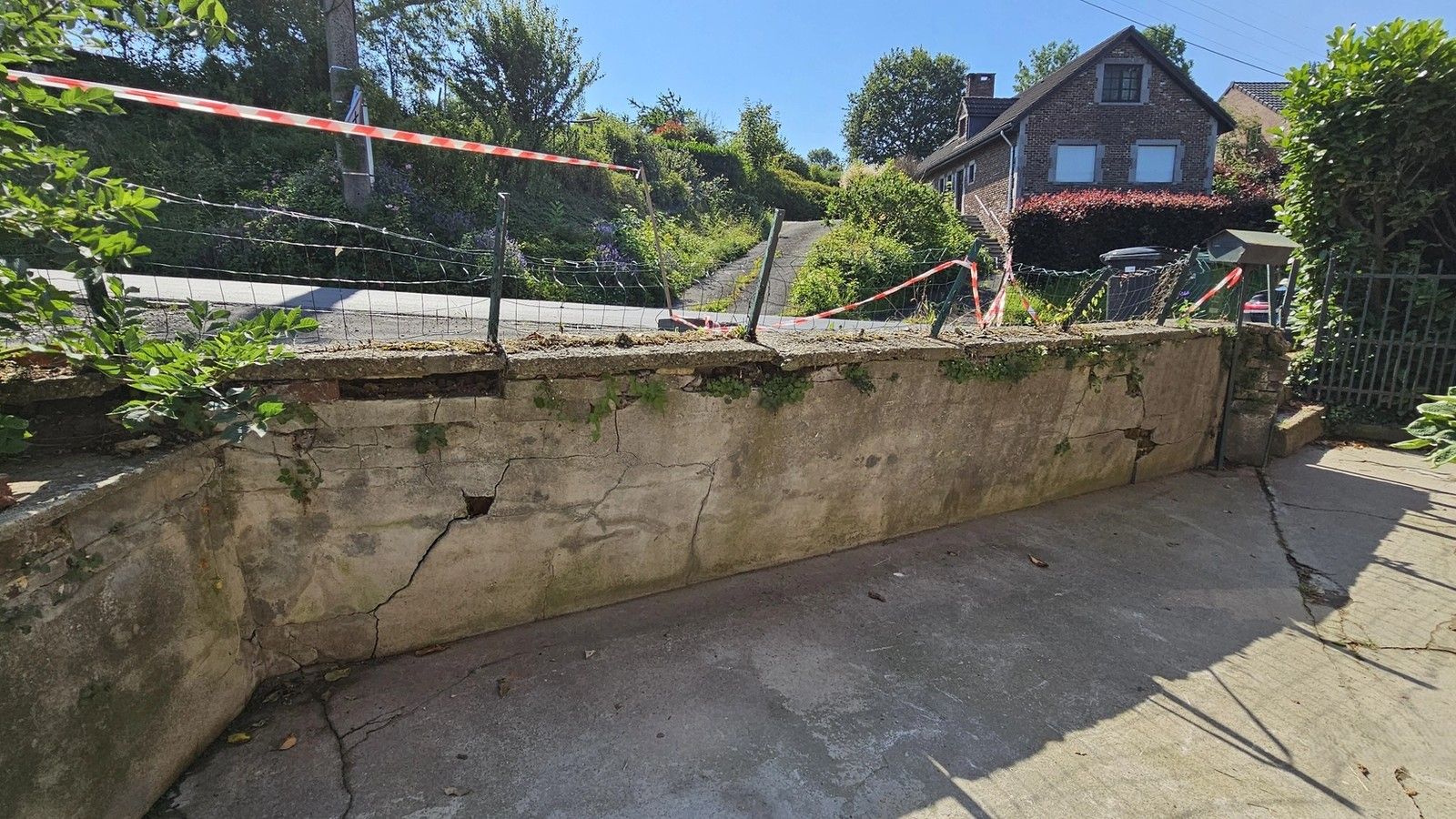Vue longitudinale du mur de soutènement fissuré à Housse, montrant la répartition des désordres sur plusieurs sections de l’ouvrage.