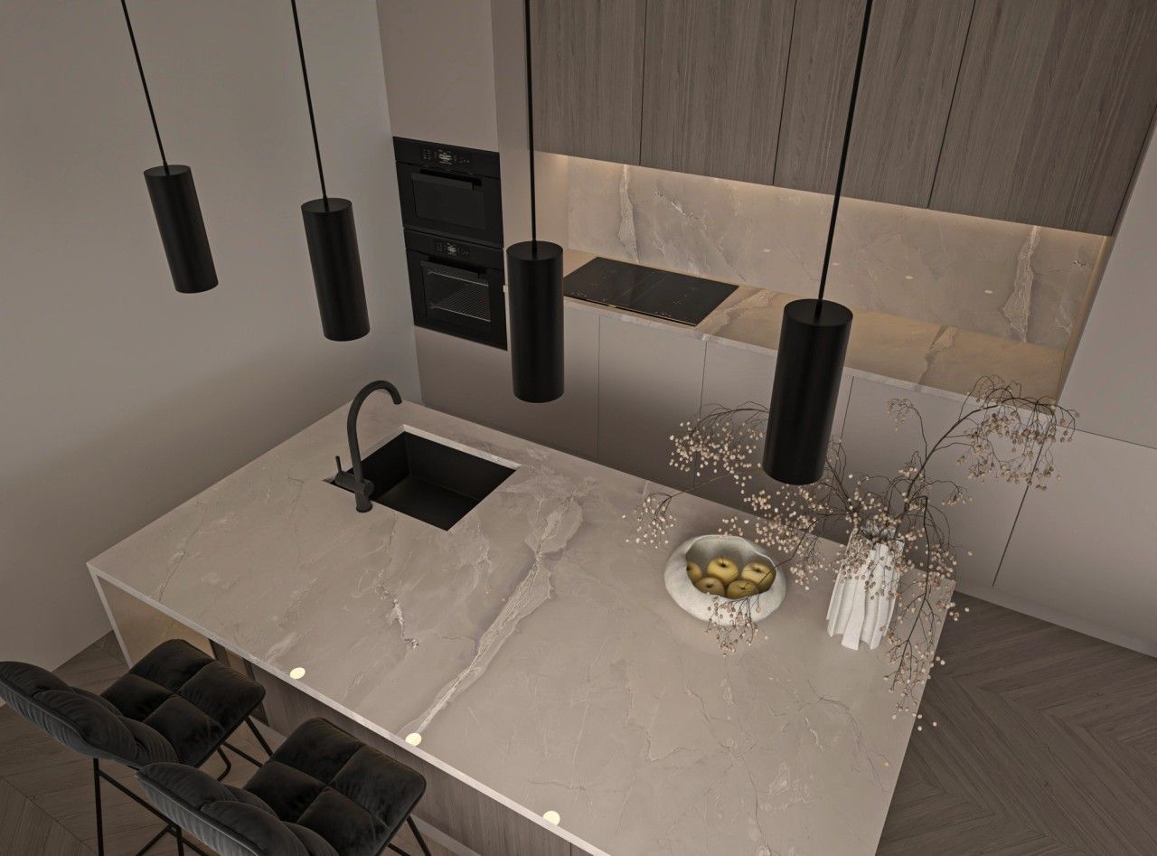 Vue en plongée sur l’îlot central d’une cuisine contemporaine à Liège, avec plan de travail en pierre claire, évier noir, suspensions cylindriques et mobilier intégré.