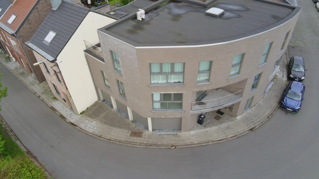 Vue aérienne de l’immeuble résidentiel à Flémalle mettant en évidence sa volumétrie courbe, sa toiture plate et son implantation à l’angle des rues.