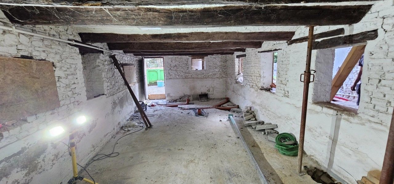 Vue intérieure du bâtiment en rénovation à Blegny, avec murs en maçonnerie existante, poutres en bois, étaiements provisoires et réseaux techniques en cours de pose.