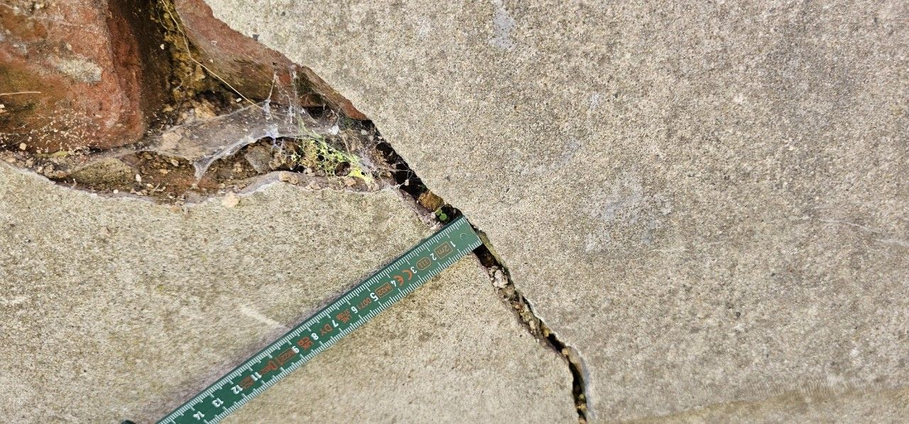 Mesure sur site d’une ouverture de fissure dans un mur de soutènement à Housse à l’aide d’un mètre gradué.
