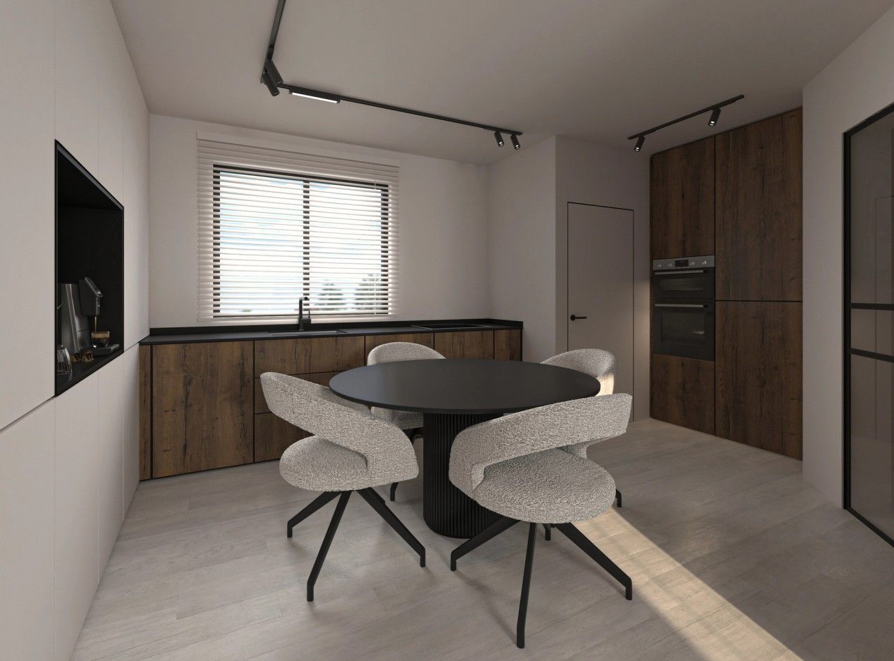 Vue intérieure de la cuisine et de l’espace repas à Herstal, avec façades en bois foncé, plan de travail noir et table ronde entourée de fauteuils clairs.