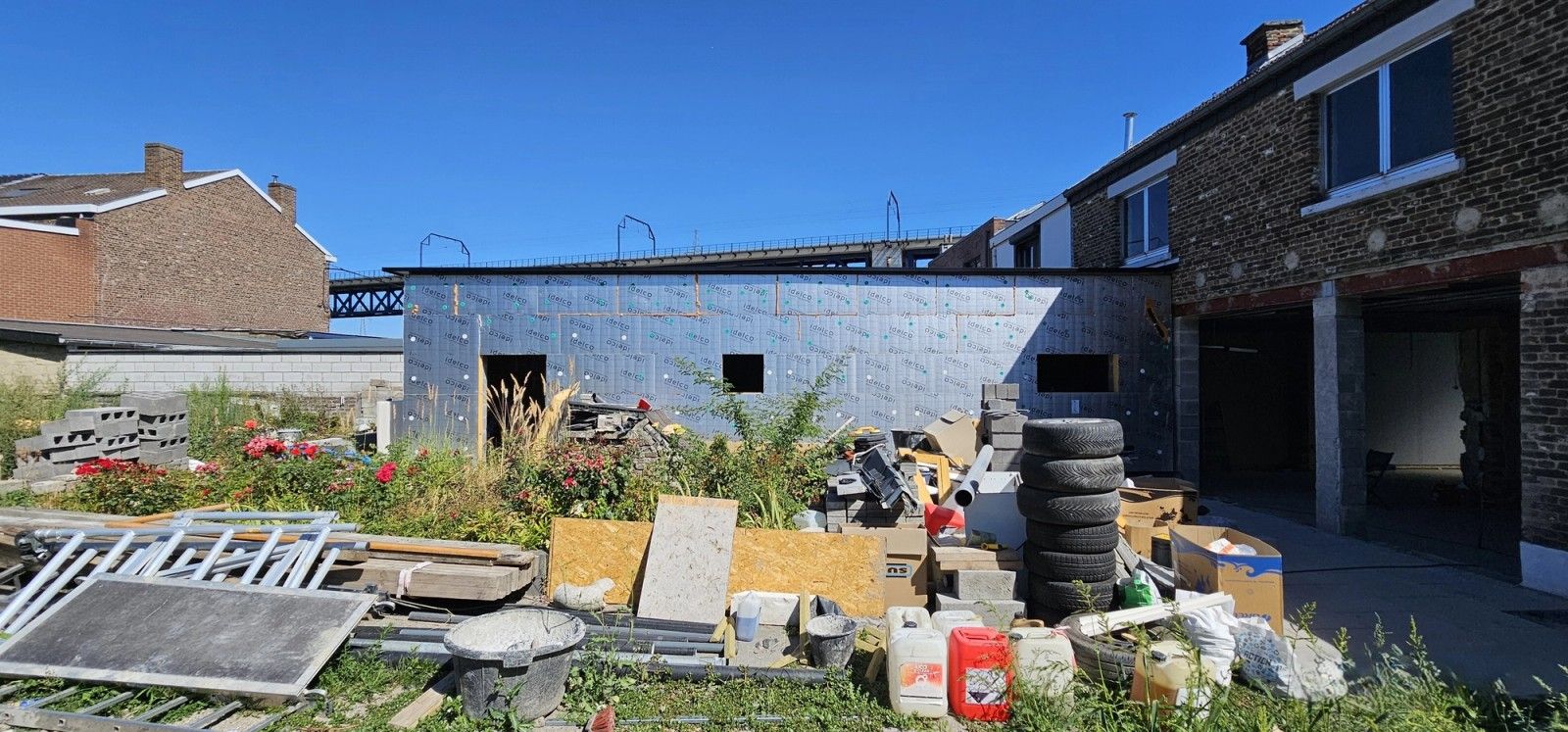 Vue du chantier depuis le jardin à Visé, montrant la nouvelle annexe arrière en cours de fermeture et une large ouverture créée dans la façade existante.