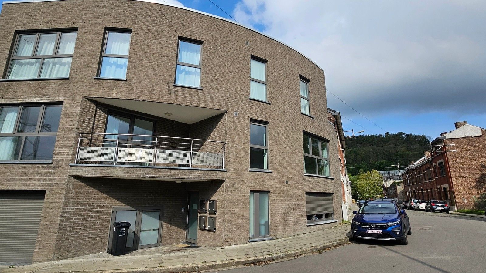 Vue depuis la rue de l’immeuble résidentiel de quatre appartements à Flémalle, avec façade courbe en briques, grandes baies vitrées et balcons intégrés.