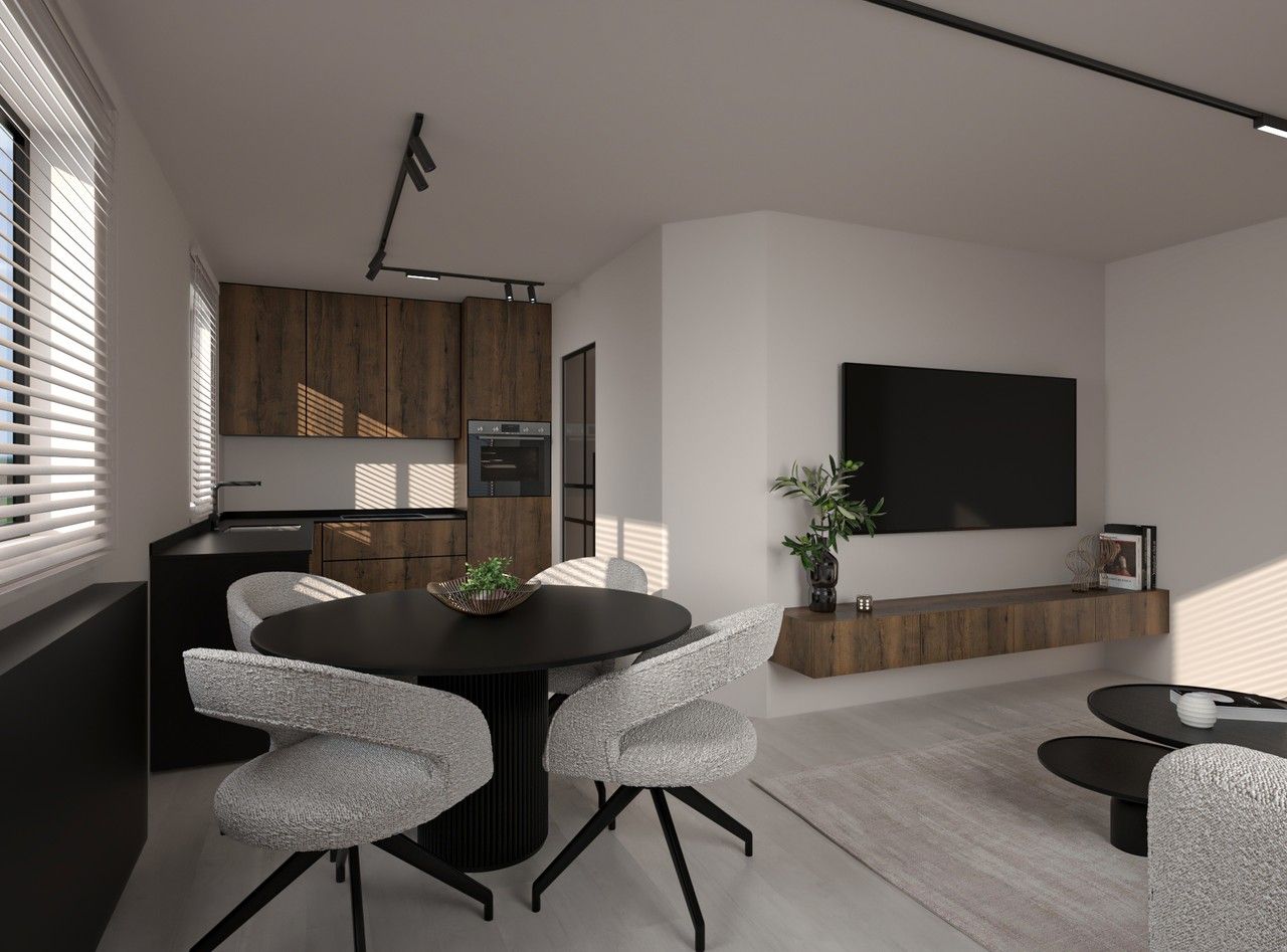 Vue intérieure de l’espace repas ouvert sur le séjour et la cuisine à Herstal, avec table ronde noire, mobilier clair et meuble TV suspendu en bois.