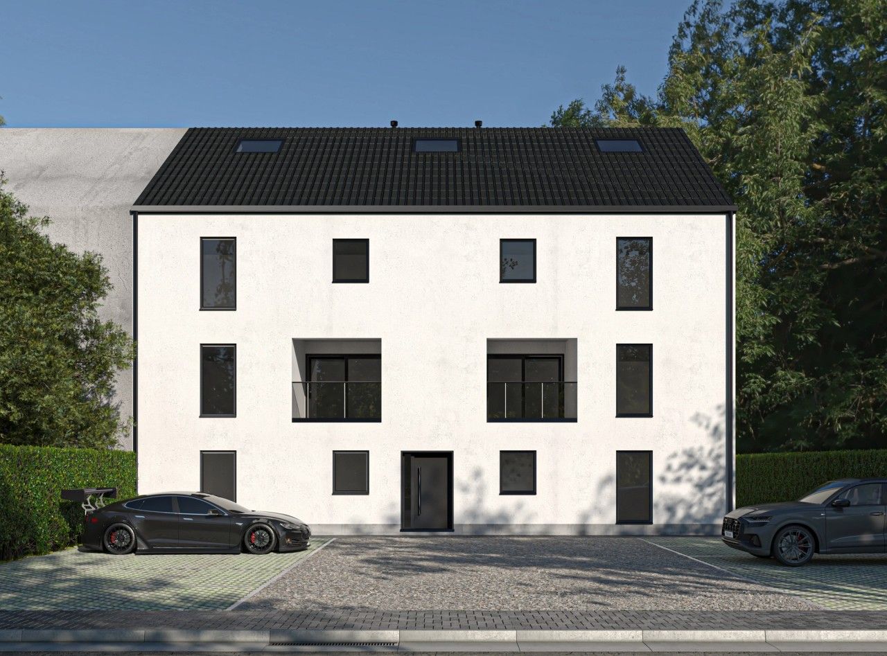Façade avant d’un immeuble résidentiel de six appartements à Oupeye, avec crépi blanc, châssis noirs, balcons en retrait et stationnements paysagers.