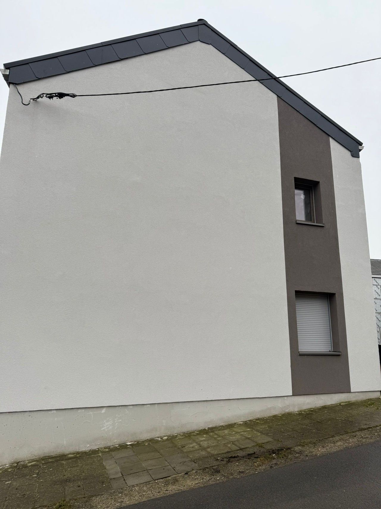 Vue du pignon rénové de l’habitation à Amay, avec isolation extérieure enduite et bande verticale contrastée autour des ouvertures.