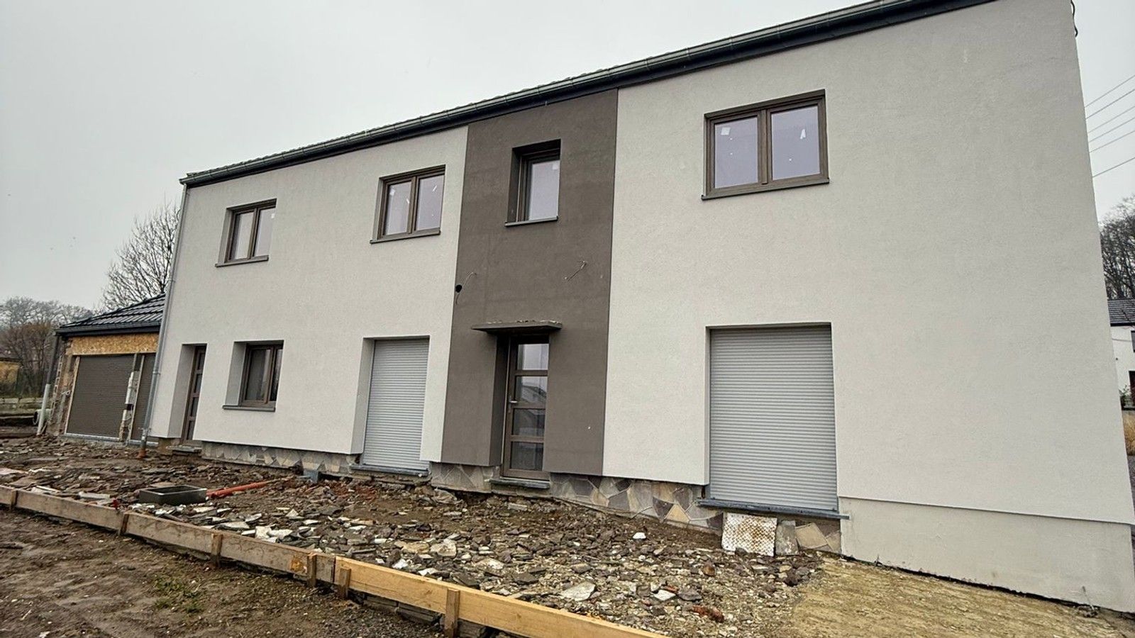 Vue d’une façade rénovée de l’habitation à Amay, avec isolation extérieure enduite, châssis remplacés et traitement contrasté de la zone d’entrée.