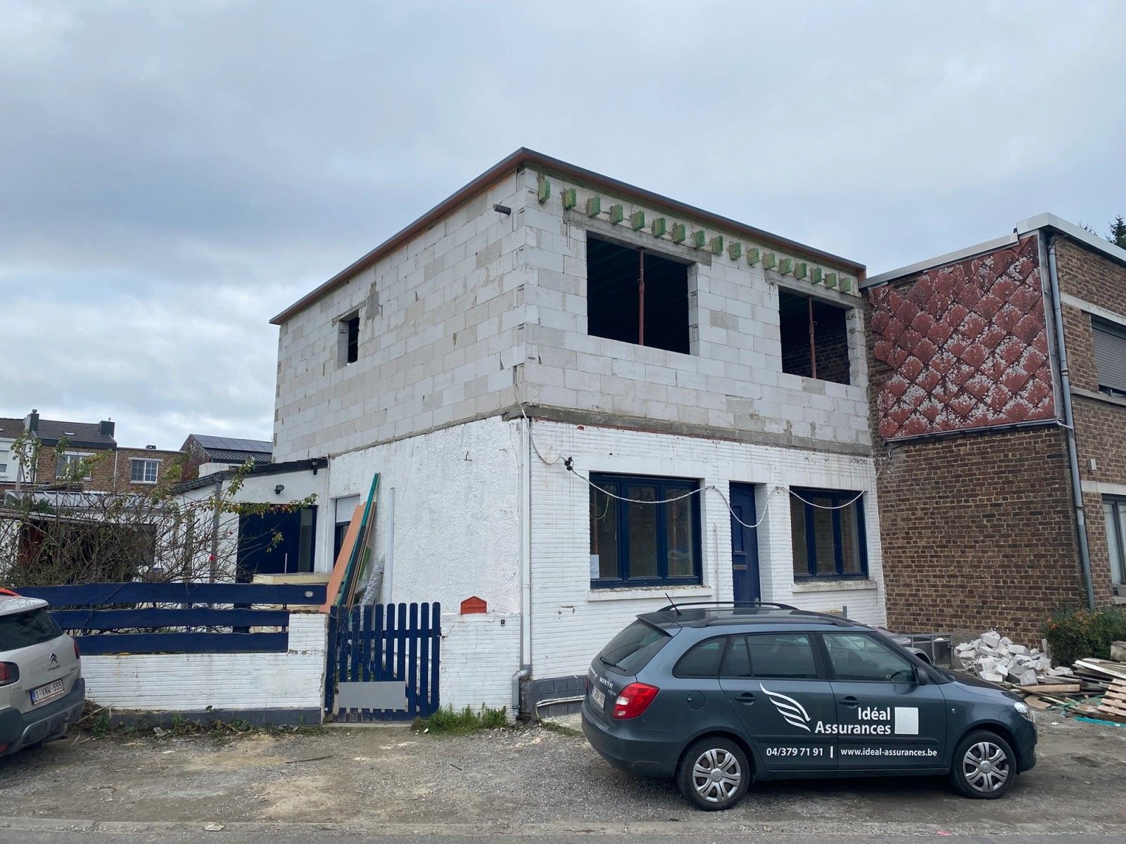 Vue de la façade avant pendant la reconstruction de l’étage d’une maison à Herstal, avec nouvelles maçonneries, toiture plate et grandes ouvertures en attente de châssis.