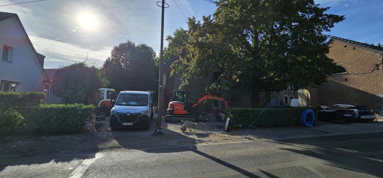 Vue générale du chantier à Blegny avec engins de terrassement, véhicules d’entreprise et accès au bâtiment existant en cours de transformation.