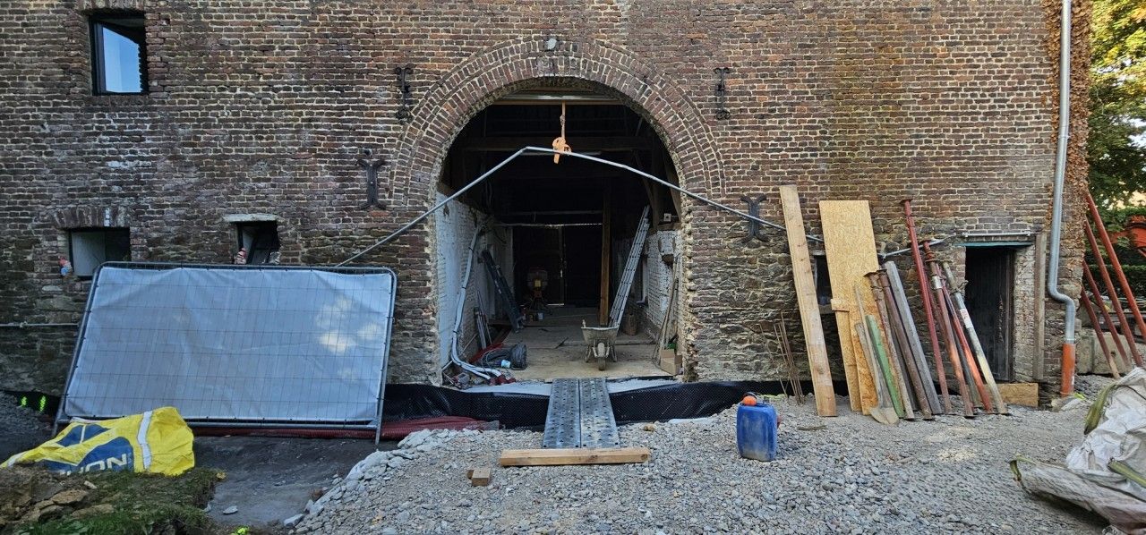 Grande baie cintrée en briques d’un bâtiment existant à Blegny pendant les travaux de transformation, avec étaiements, matériaux et zone de chantier.