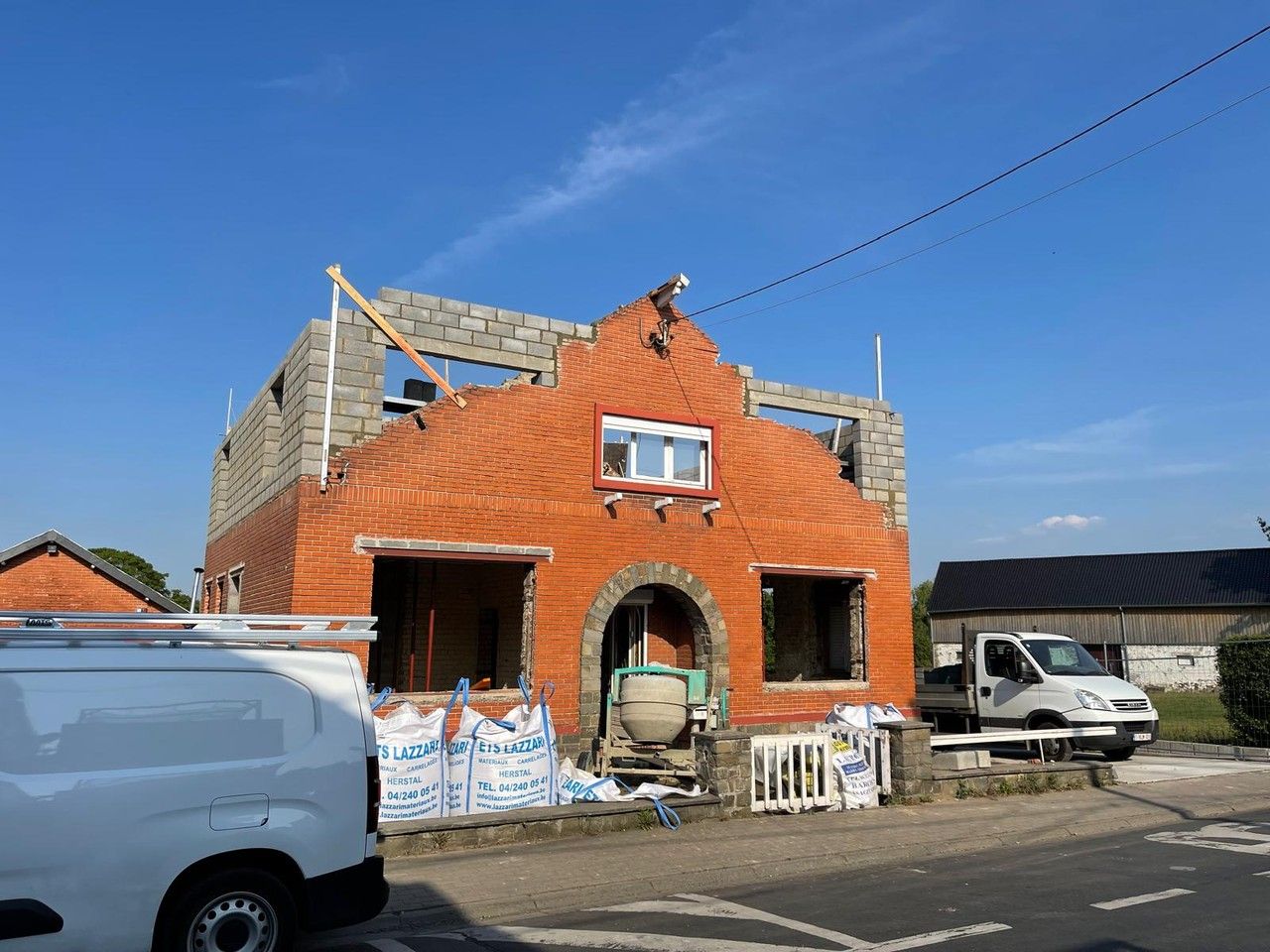 Vue oblique de l’habitation existante à Vottem avant travaux, montrant la façade avant en briques et le volume latéral.