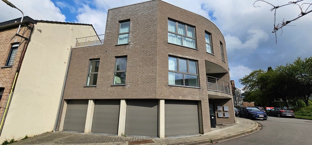 Vue latérale de l’immeuble de quatre appartements à Flémalle, montrant la façade en briques, les garages intégrés et les logements aux étages.