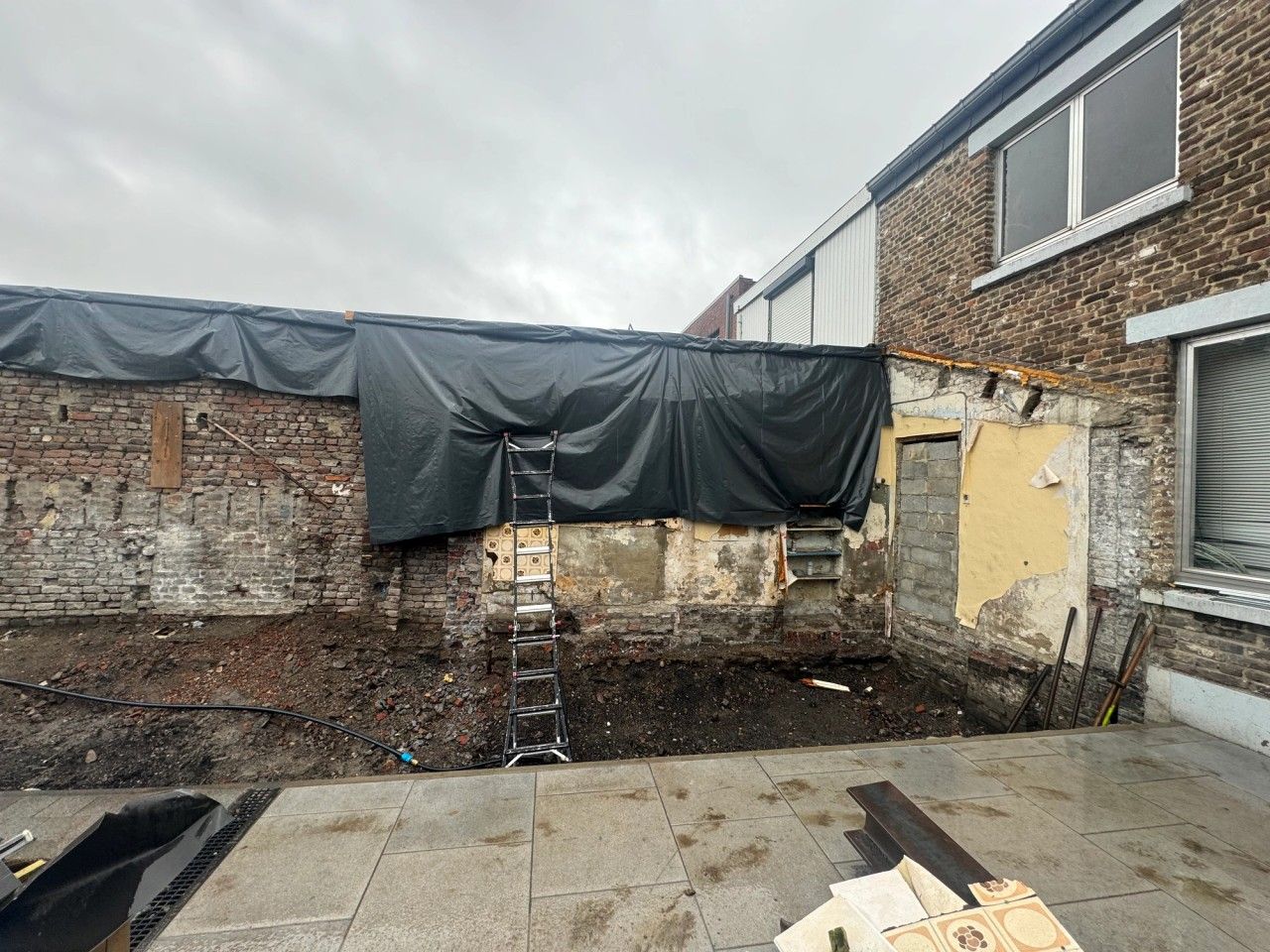Chantier de rénovation à Visé après démolition de l’ancienne annexe arrière, avec maçonneries existantes mises à nu et terrasse conservée.