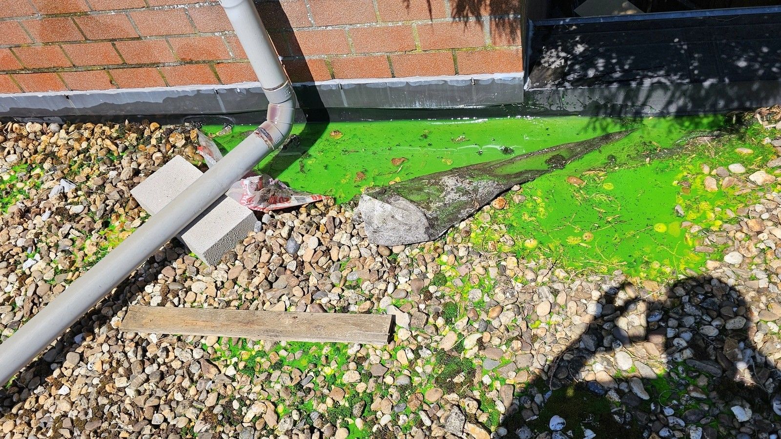 Essai de traçage sur la toiture plate lestée d’un garage à Ans, avec produit fluorescent appliqué autour de la descente d’eau et au pied de la façade.