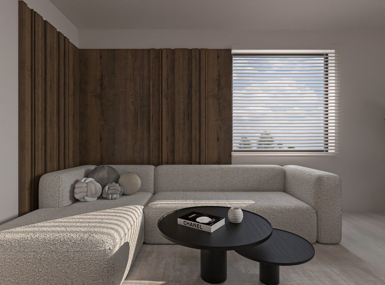 Vue du séjour à Herstal avec canapé d’angle clair, tables basses noires, mur décoratif en bois et lumière naturelle filtrée par des stores horizontaux.