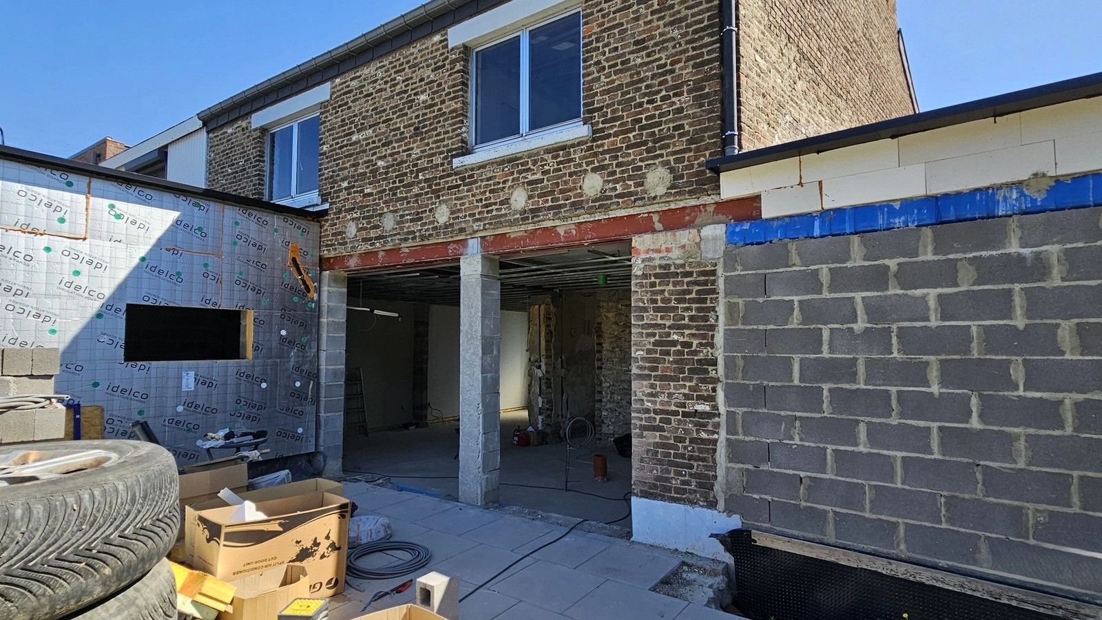 Vue du chantier arrière d’une maison à Visé, montrant une large ouverture créée dans la façade existante, soutenue par une poutre métallique, entre les nouvelles extensions en maçonnerie.