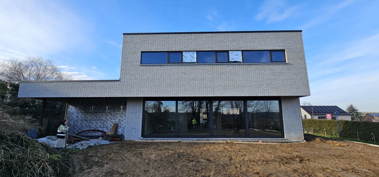Chantier d’une maison contemporaine neuve à Oupeye montrant la façade côté jardin en briques claires, les grandes baies vitrées et le bandeau de fenêtres à l’étage.