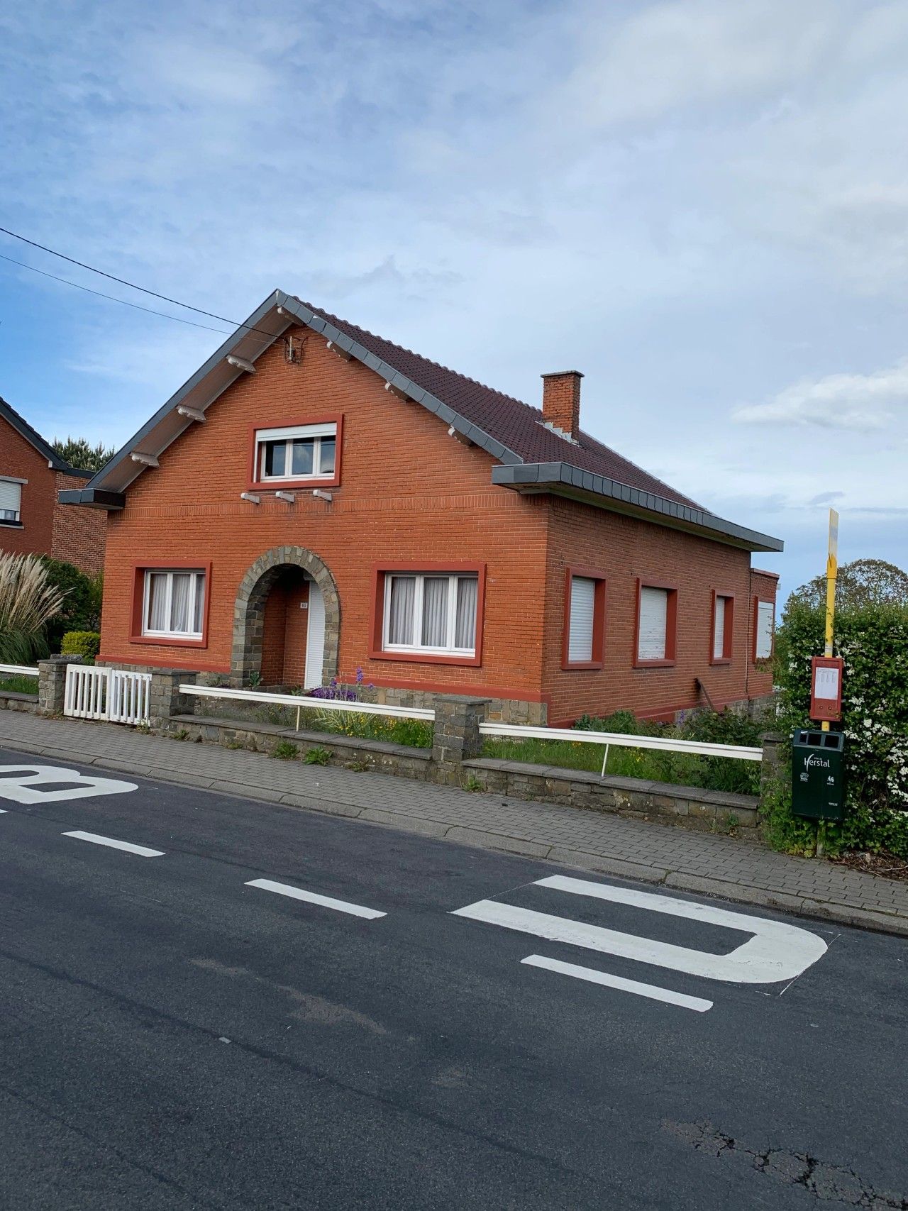 Vue frontale de l’habitation existante à Vottem avant rénovation énergétique, avec façade en briques rouges, soubassement en pierre et entrée cintrée.