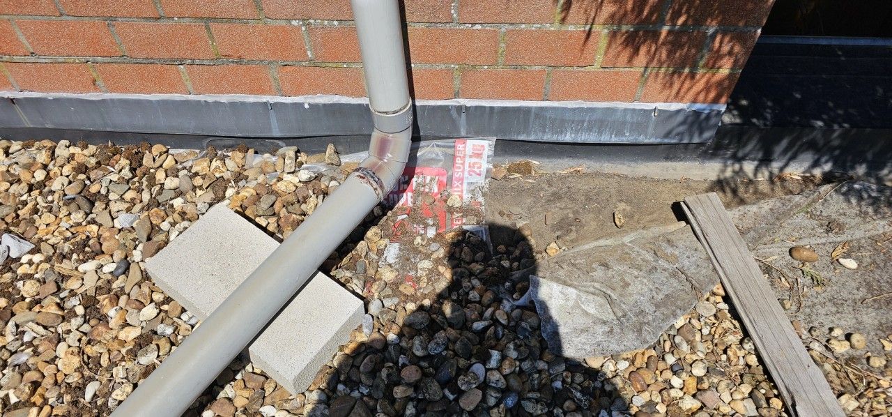 Vue de la toiture plate lestée d’un garage à Ans, avec descente d’eau pluviale, membrane d’étanchéité et raccord en pied de façade en briques.